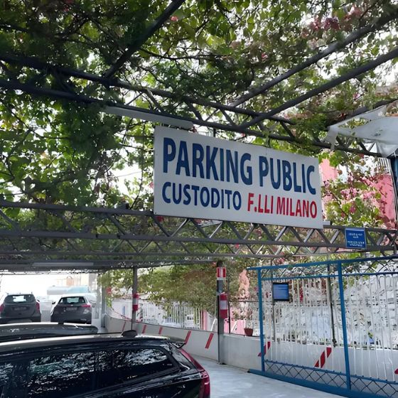 Entrance of the guarded Parcheggio Fratelli Milano in Positano, showing parked cars under a shaded pergola.