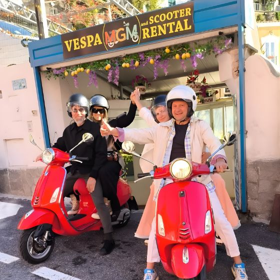 Happy couple smiling on a red Vespa outside the MGM Scooter Rental shop in Positano.