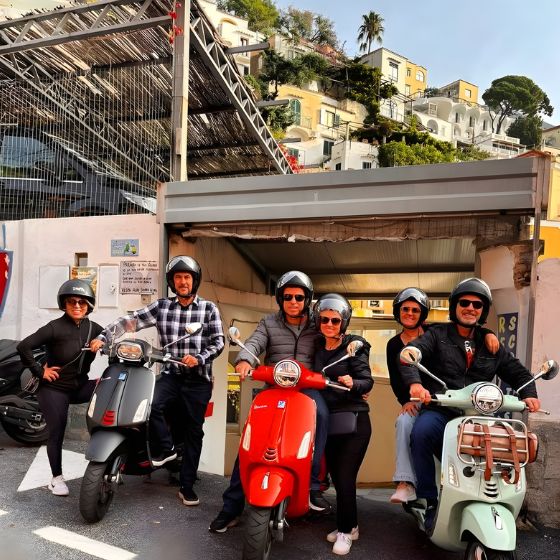A large group of happy friends sitting on colourful rented Vespas ready for a tour in Positano.